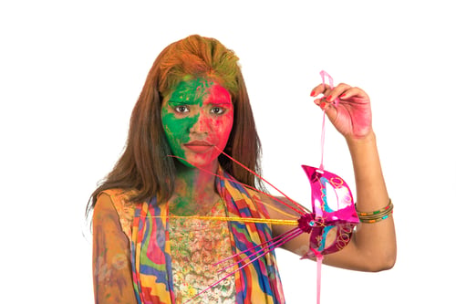 Preview: Girl With Colorful Face Holding Carnival Mask And Celebrating Holi.