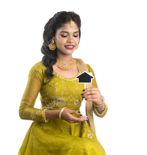 Preview: Happy Indian Traditional Young Woman Holding A Little House Cutout Board In Her Hands On A White