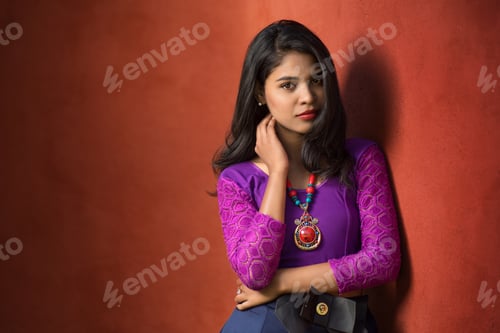 Preview: Beautiful Indian Young Girl Posing Outdoors On Red Wall Background.