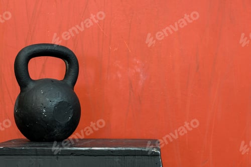 Preview: Black Kettle Bell On A Black Jump Box, Against A Red Wall