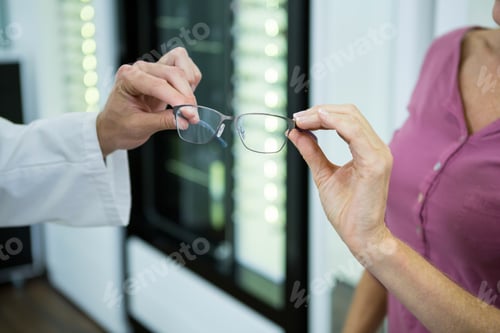 Preview: Mid Section Of Optometrist Giving Spectacles To Customer In Optical Store