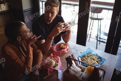 Preview: Happy Couple Interacting While Having Burger In Restaurant