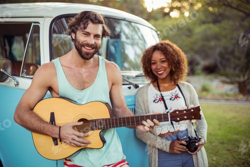 Preview: Man Playing Guitar Near Campervan While Woman Standing Beside Him On A Sunny Day