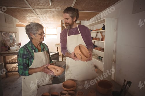Preview: Male And Female Potter Examining A Pot In Pottery Workshop