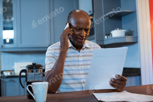 Preview: Close Up Of Man Reading Document Walking Talking On Phone In Kitchen At Home