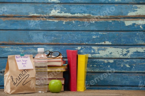 Preview: Stack Of Books, Apple, Water Bottle, Spectacles And Lunch Bag Against Blue Wooden Background