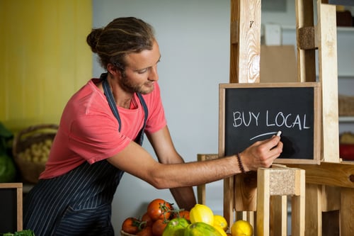 Male Staff Writing On Slate Board In Organic Section Of Supermarket