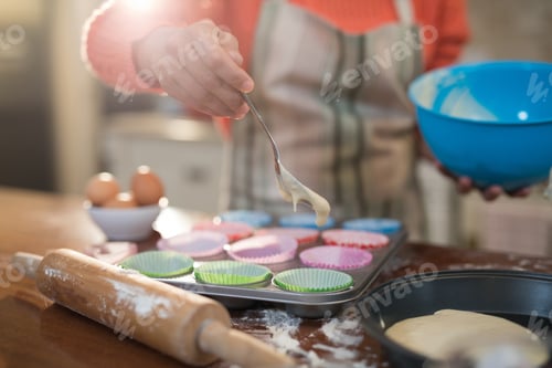 Preview: Mid Section Of Woman Putting Muffin Batter In Paper Case In Baking Tray