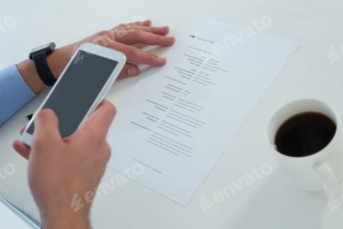 Preview: Cropped Hands Of Businessman Using Mobile Phone While Holding Document At Table