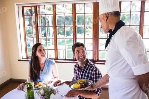 Preview: Male Chef Serving Food To Young Couple Sitting In A Restaurant