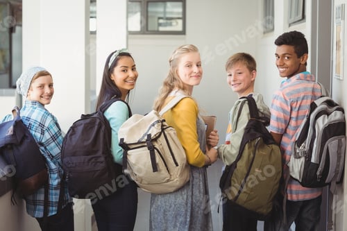 Visualização: Retrato de estudantes sorridentes em pé com caderno e mochila escolar no corredor da escola