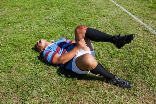 Preview: Full Length Of Rugby Player With Injured Knee Lying On Field During Sunny Day