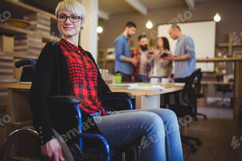Preview: Portrait Of Confident Woman On Wheelchair While Colleagues In Background At Creative Office