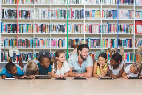 Preview: Teacher And Kids Lying On Floor Using Digital Tablet In Library At Elementary School