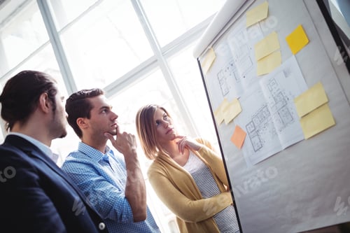 Preview: Thoughtful Business People Looking At Blueprints On Board In Creative Office