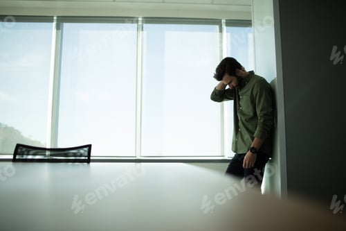Preview: Depressed Businessman Standing By Window In Office