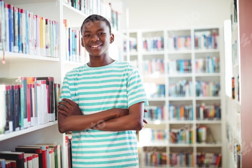 Preview: Portrait Of Happy Schoolboy Standing With Arms Crossed In Library At School