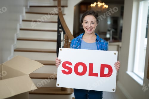 Preview: Woman Standing In The Living Room Holding Sold Sign At Home