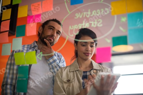 Preview: Female Executive Using Digital Tablet While Male Executive Looking At Sticky Notes In Office