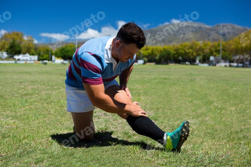 Preview: Young Rugby Player Stretching On Grassy Field On Sunny Day