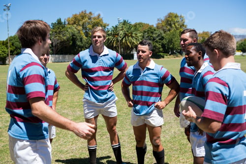 Preview: Rugby Team Discussing While Standing At Playing Field On Sunny Day