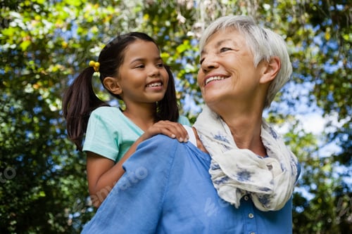 Preview: Low Angle View Of Happy Grandmother Giving Piggyback To Granddaughter Against Trees At Backyard
