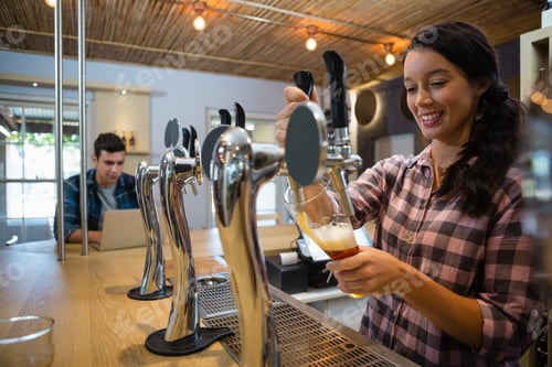 Preview: Young Smiling Barmaid Pouring Beer From Tap In Glass At Restaurant