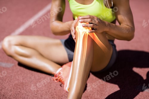 Preview: Low Section Of Female Athlete Suffering From Knee Pain While Sitting On Track During Sunny Day