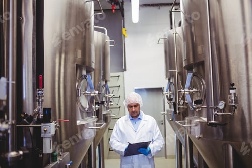 Preview: Front View Of Manufacturer Writing While Standing Amidst Storage Tanks At Brewery
