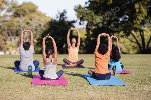 Preview: Female Instructor Teaching Children Stretching While Sitting On Mat At Park