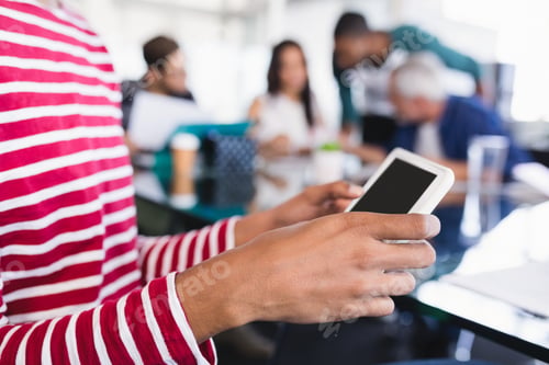 Preview: Midsection Of Businesswoman Using Phone While Sitting With Colleagues At Desk In Office
