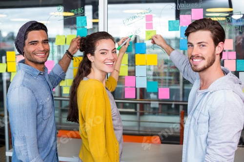 Preview: Portrait Of Smiling Executives Writing On Sticky Note On Glass Wall In Office