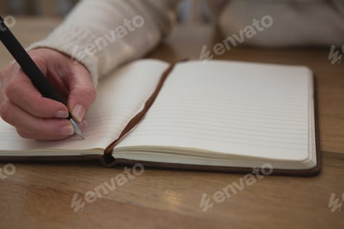 Preview: Close-Up Of Woman Writing On A Diary At Home