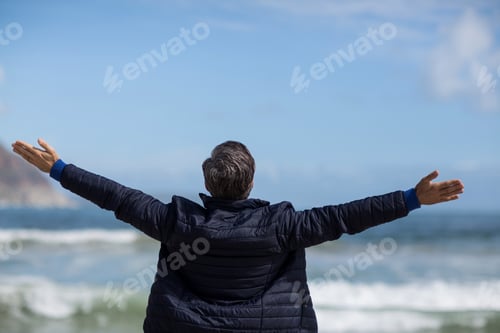 Preview: Rear View Of Mature Man With Arms Outstretched Standing On The Beach