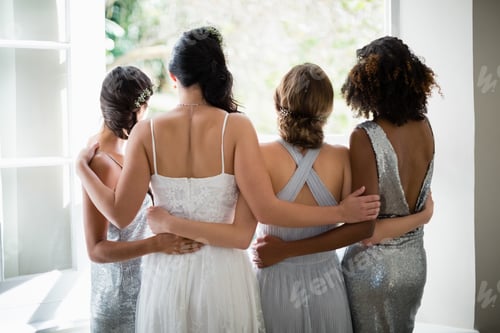 Preview: Rear View Of Bride And Bridesmaids Standing Together Near Window At Home