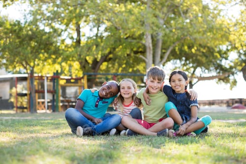 Preview: Portrait Of Happy Children With Arms Around Sitting On Grassy Field At Park