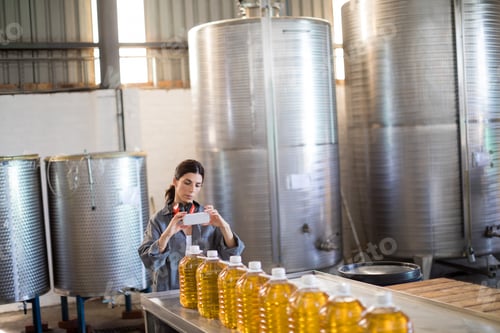 Preview: Female Worker Taking Photo Of Oil Bottles From Mobile Phone In Oil Factory
