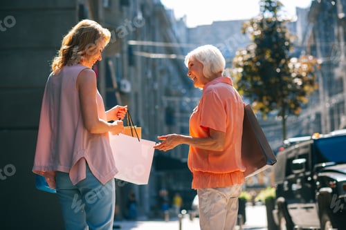 Preview: Happy Elderly Woman Smiling And Looking At The Adult Daughter With Shopping Bags