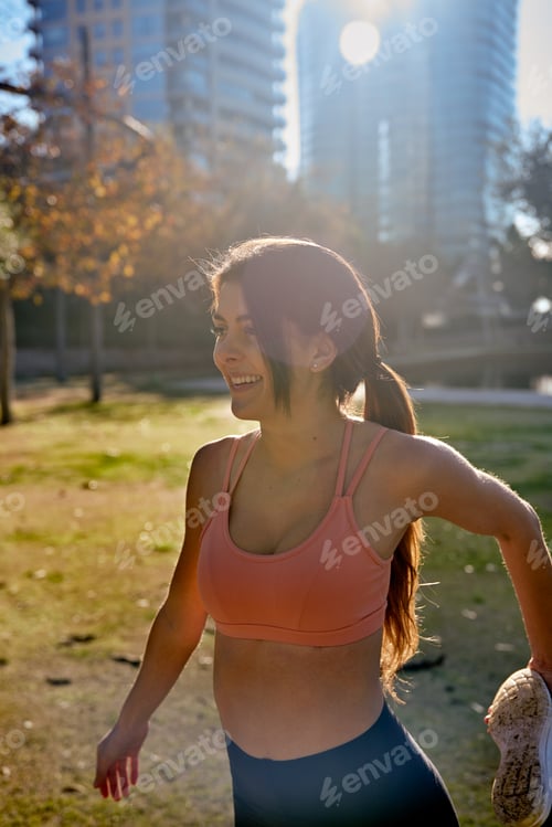 Preview: Young Woman Smiles And Holds Her Leg Behind Her As She Does Stretching Exercises In The Park