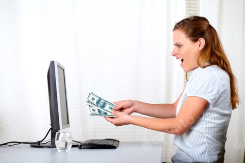 Preview: Portrait Of A Ambitious Excited Blonde Girl Holding Plenty Of Cash Money Looking On Computer Screen