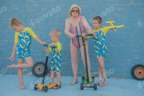 Preview: Elderly Woman In Striped Swimsuit, Sunglasses And Elegant Hat Riding Scooter Against Brick Wall