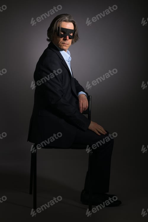 Preview: A Mysterious Man In An Elegant Suit And Black Mask Is Sitting On A Chair On A Black Background.