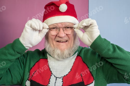 Preview: Elderly Man With Gray Beard And Glasses In Santa Claus Hat With Red Bag Filled With Presents Poses