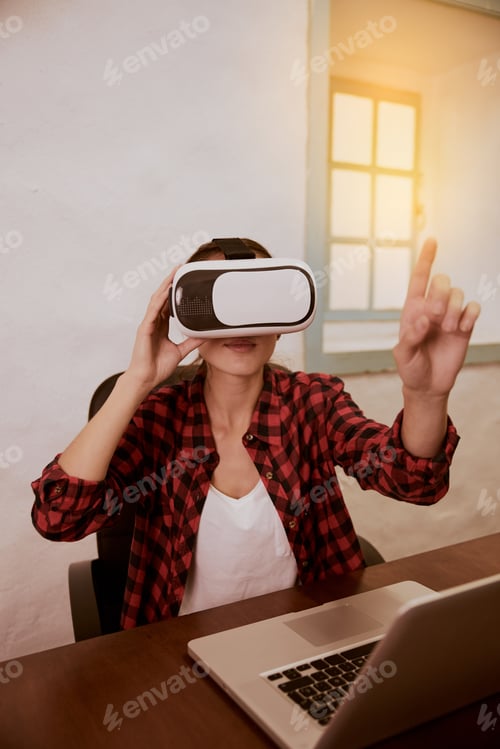 Preview: Young Woman With A 3D Viewer To Her Eyes Sitting With Her Laptop Facing The Camera While Holding