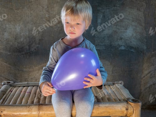 Preview: Funny Blond Kid In Gray Clothes Holds Purple Ball In His Hands