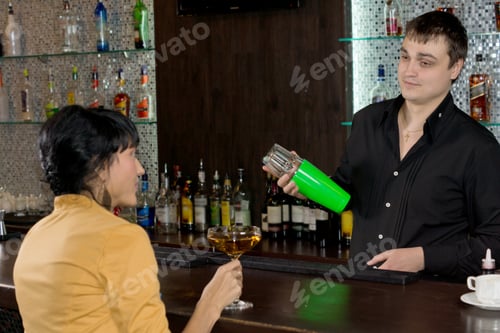 Preview: Handsome Young Barman Mixing A Martini Cocktail In A Shaker While Chatting To A Woman Customer