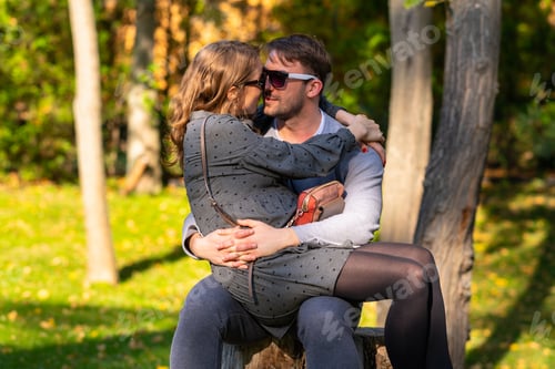 Preview: Happy Pregnant Young Woman Sitting On Her Husbands Lap As They Relax Outdoors In An Autumn Park