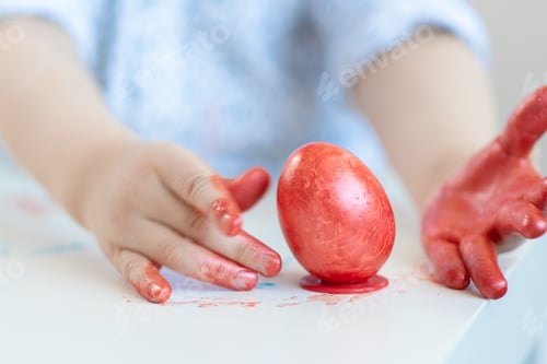 Preview: A Child In A Shirt Puts A Red Easter Egg On A Stand With Stained Hands Which He Painted And
