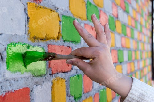 Preview: Young Caucasian Shapely Woman Paints A Brick Wall With Paint Brush In Different Colors. Red, Blue