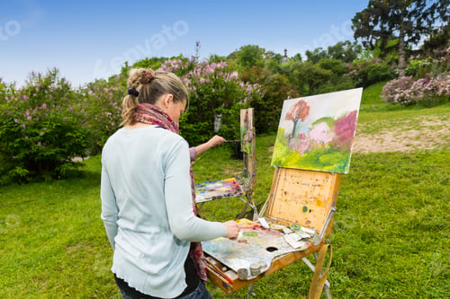 Preview: Back View Of A Concentrated Female Painter Working On A Trestle And Easel Painting With Oils And